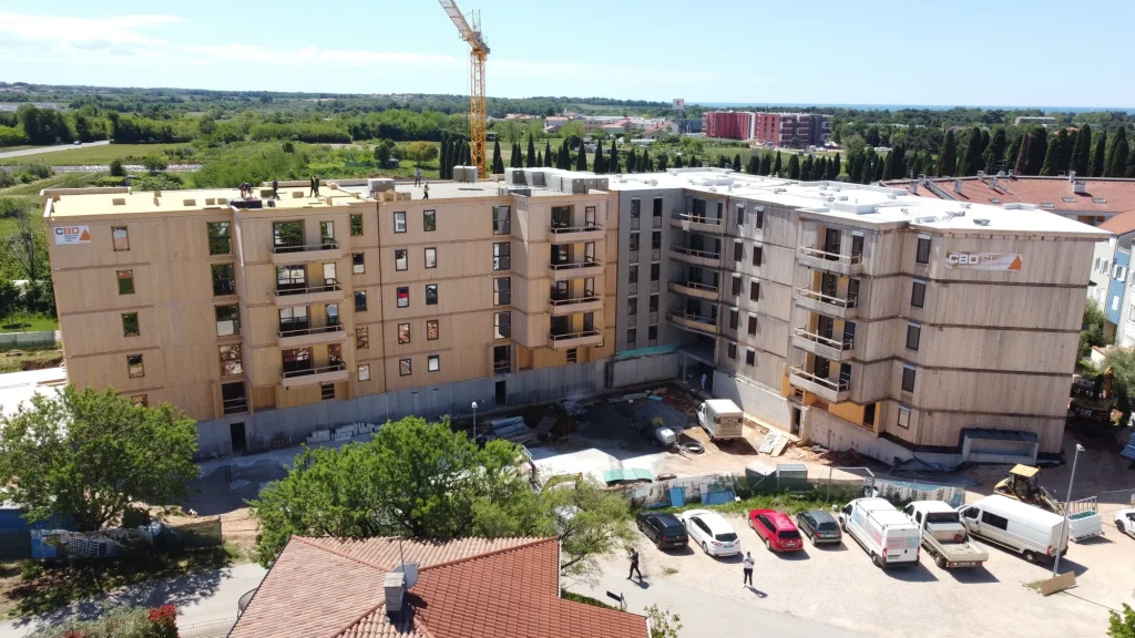 Aerial view of a large timber building under construction, surrounded by residential buildings and greenery