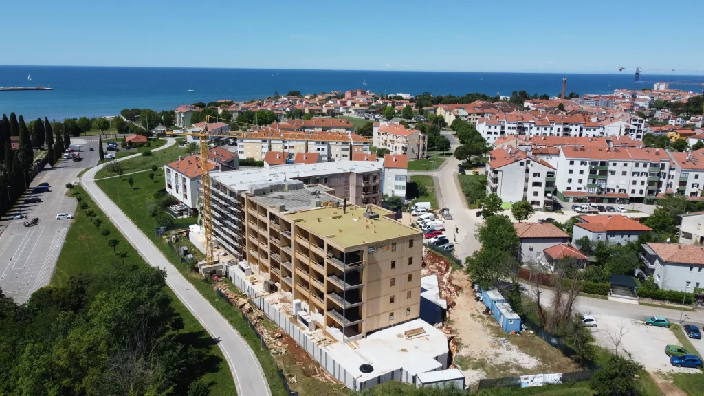 Zračni posnetek velike lesene stavbe v gradnji, obdane s stanovanjskimi objekti in zelenjem